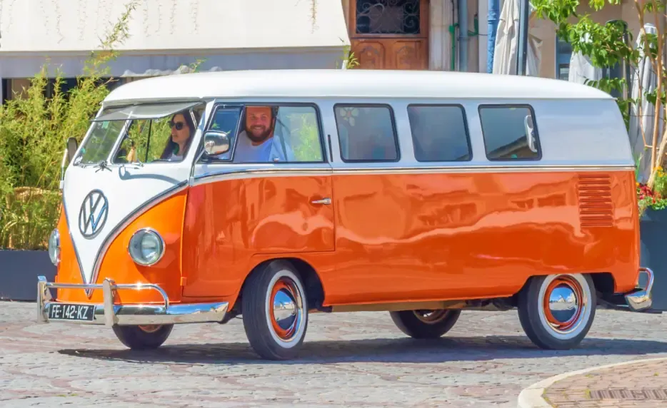 Photo du van Volkswagen orange en train de rouler sur une petite place